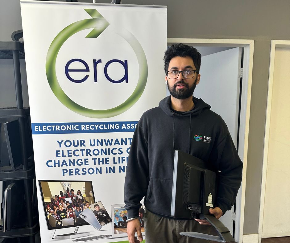 A recipient holding a refurbished laptop beside an ERA banner